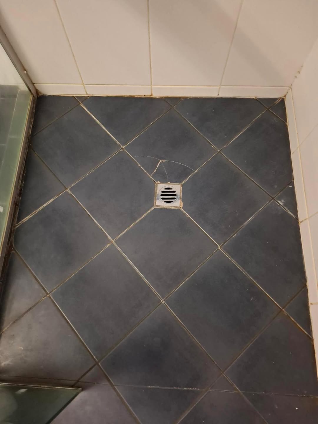 Before restoration: dark shower floor with stained grout around drain